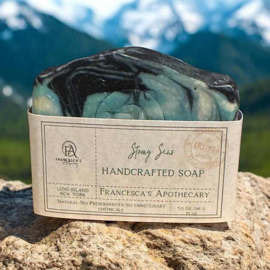 Handcrafted Stormy Seas Soap with citrus, wood, and floral fragrance, on a rock with mountains in background.