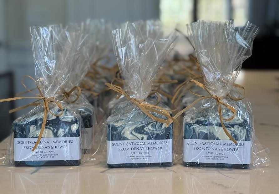 Custom wedding shower favor soaps with spearmint and eucalyptus fragrance, featuring three shades of blue and white design, wrapped in biodegradable glitter and mica, topped with a shell, and labeled with custom messages.