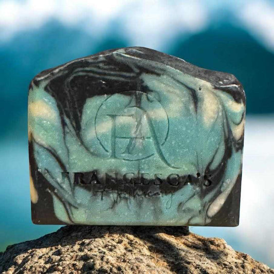 Stormy Seas Soap with citrus, woody fragrance on a rocky shore backdrop.