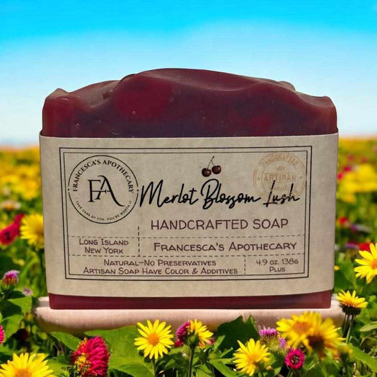 Handcrafted Merlot Blossom Lush soap with floral fruity scent, set against a field of vibrant flowers.
