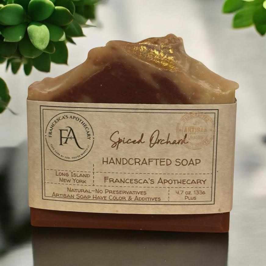 Handcrafted spicy fruit soap labeled "Spiced Orchard" with notes of cranberry, apple, ginger, and spices, elegantly displayed with green accents.