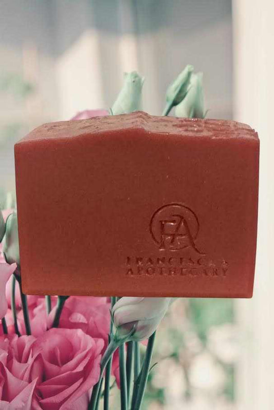 Floral fruity soap block with brand logo, surrounded by pink flowers.